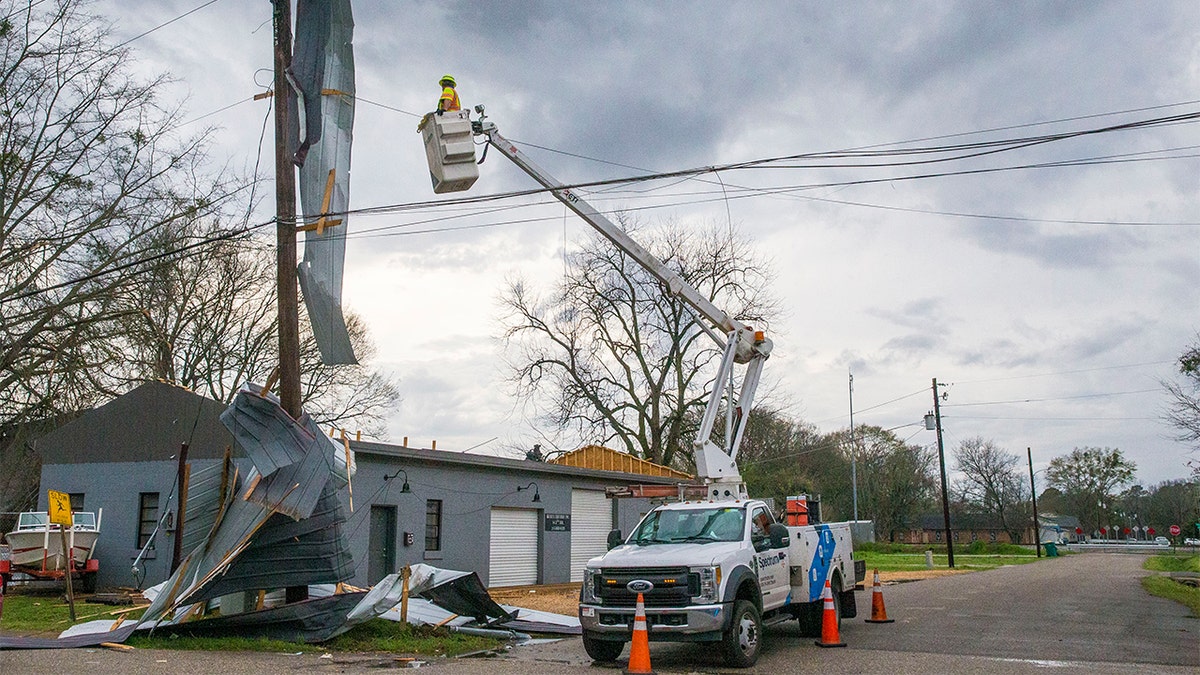 A utility worker looks to repair lines with the roof of Kelley Electric draped on the lines after downtown Moundville was hit by severe weather, Wednesday, March 17, 2021, in Moundville, Ala. Possible tornadoes knocked down trees, toppled power lines and damaged homes in rural Chilton County and the Alabama communities of Burnsville and Moundville, where power was out and trees blocked a main highway. (AP Photo/Vasha Hunt)