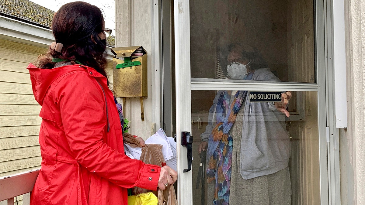 Senior citizen Barbara Bender answers the door for Store to Door employee Nancy Murphy in Portland, Ore., as she delivers an order of groceries for the nonprofit on Feb. 25, 2021. (AP Photo/Gillian Flaccus)