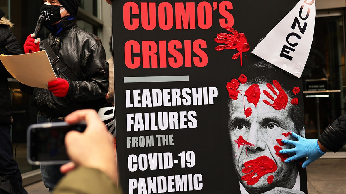 A person places his red painted hands on a poster of Gov. Andrew Cuomo's book as people gather outside of his NYC office to protest against cuts to health care on March 01, 2021 in New York City. (Photo by Michael M. Santiago/Getty Images)