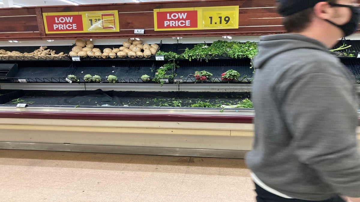 A shopper passes by the remnants of the produce display late Thursday in a grocery store in south Denver. (AP)