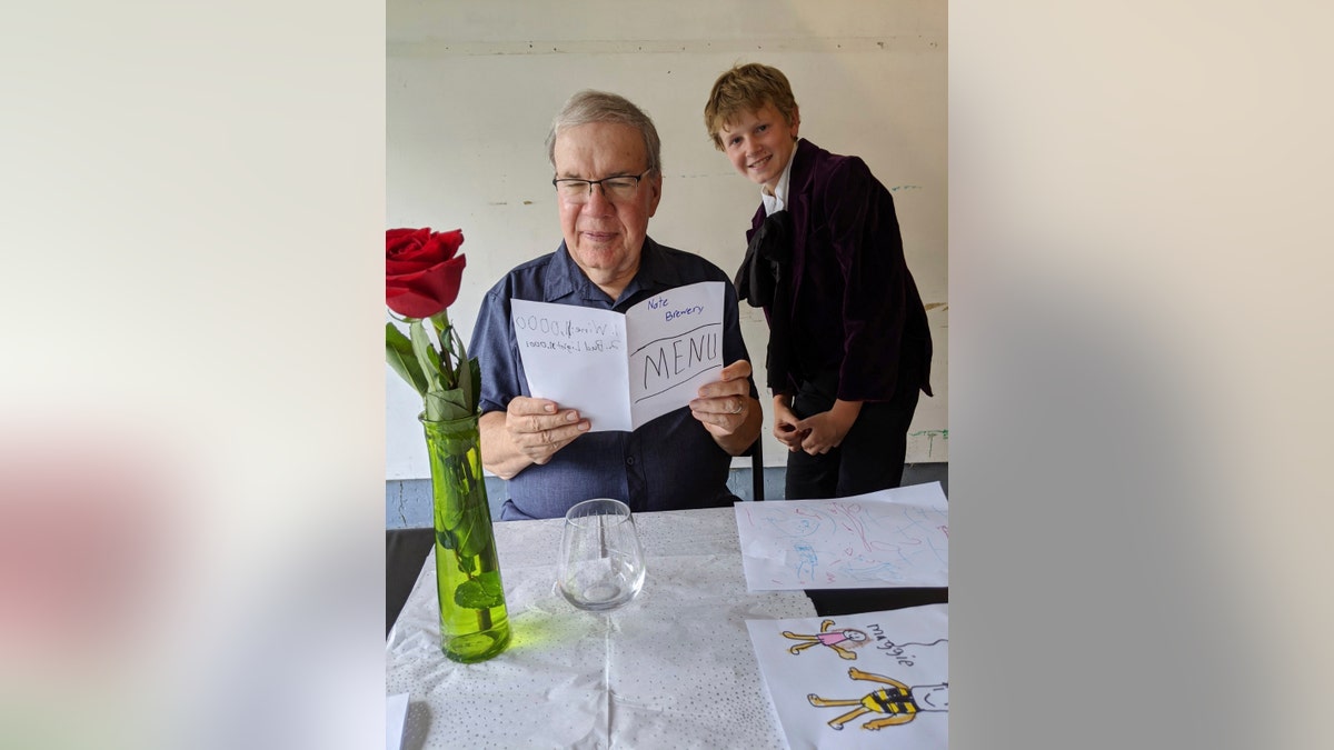 In this Aug, 2020, photo provided by courtesy of Nancy Peters, Joe Peters reads the menu on his birthday in a garage served by grandson, Nate Hoying, right, in Cincinnati.