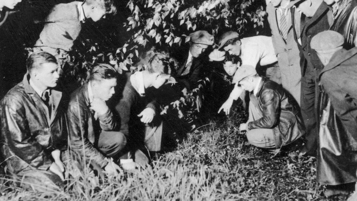 Newsmen and spectators are watching as a young man points to the spot where the body of 19-month-old baby Charles A. Lindbergh Jr., was found in a shallow grave, near Mount Rose, N.J., on May 12, 1932. The infant son of world-famed aviator Charles Lindbergh was kidnapped on March 1, 1932, and found dead, only four-and-a-half miles away from the Lindbergh estate. (AP Photo)