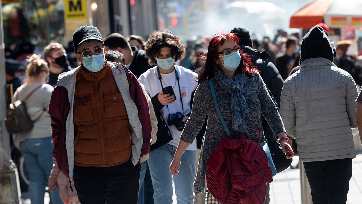People wearing masks walk in Times Square on the first day of spring on March 20, 2021m in New York City. 