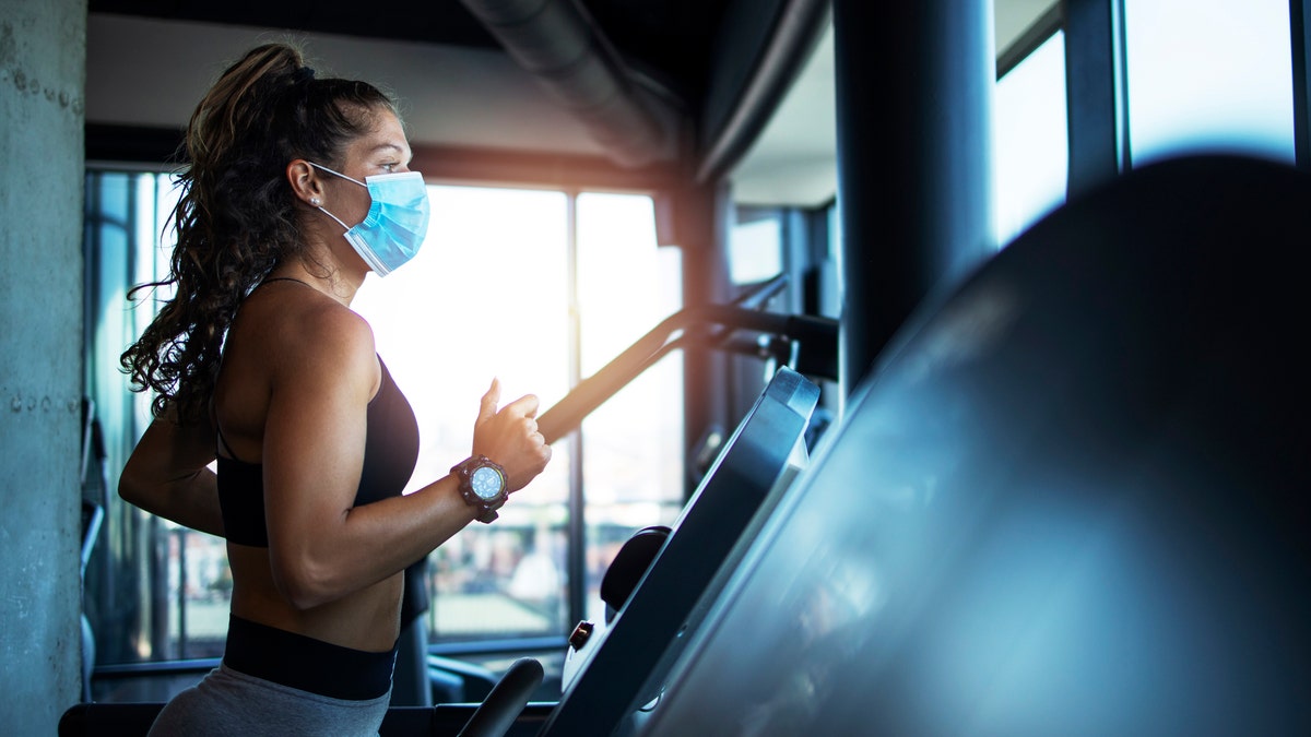 Sportswoman training on treadmill in gym and wearing face mask to protect herself against coronavirus during global pandemic of covid-19 virus.