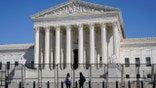 FILE - In this March 21, 2021, file photo people view the Supreme Court building from behind security fencing on Capitol Hill in Washington after portions of an outer perimeter of fencing were removed overnight to allow public access. A Supreme Court case being argued this week amid March Madness could erode the difference between elite college athletes and professional sports stars. (AP Photo/Patrick Semansky, File)