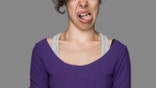 Disgusted young woman sticking out tongue over isolated gray background. Image taken with Hasselblad H3D camera system and developed from camera RAW.