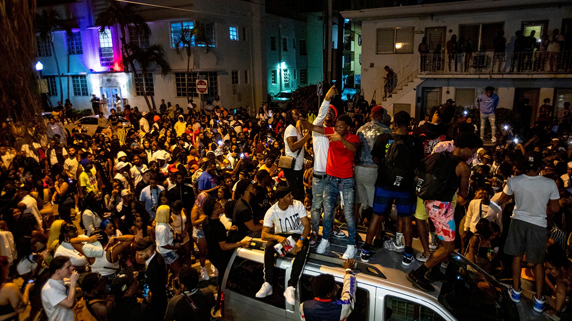 Crowds defiantly gather in the street while a speaker blasts music an hour past curfew in Miami Beach, Florida, on Sunday, March 21, 2021. An 8 p.m. curfew has been extended in Miami Beach after law enforcement worked to contain unruly crowds of spring break tourists. (Daniel A. Varela/Miami Herald via AP)