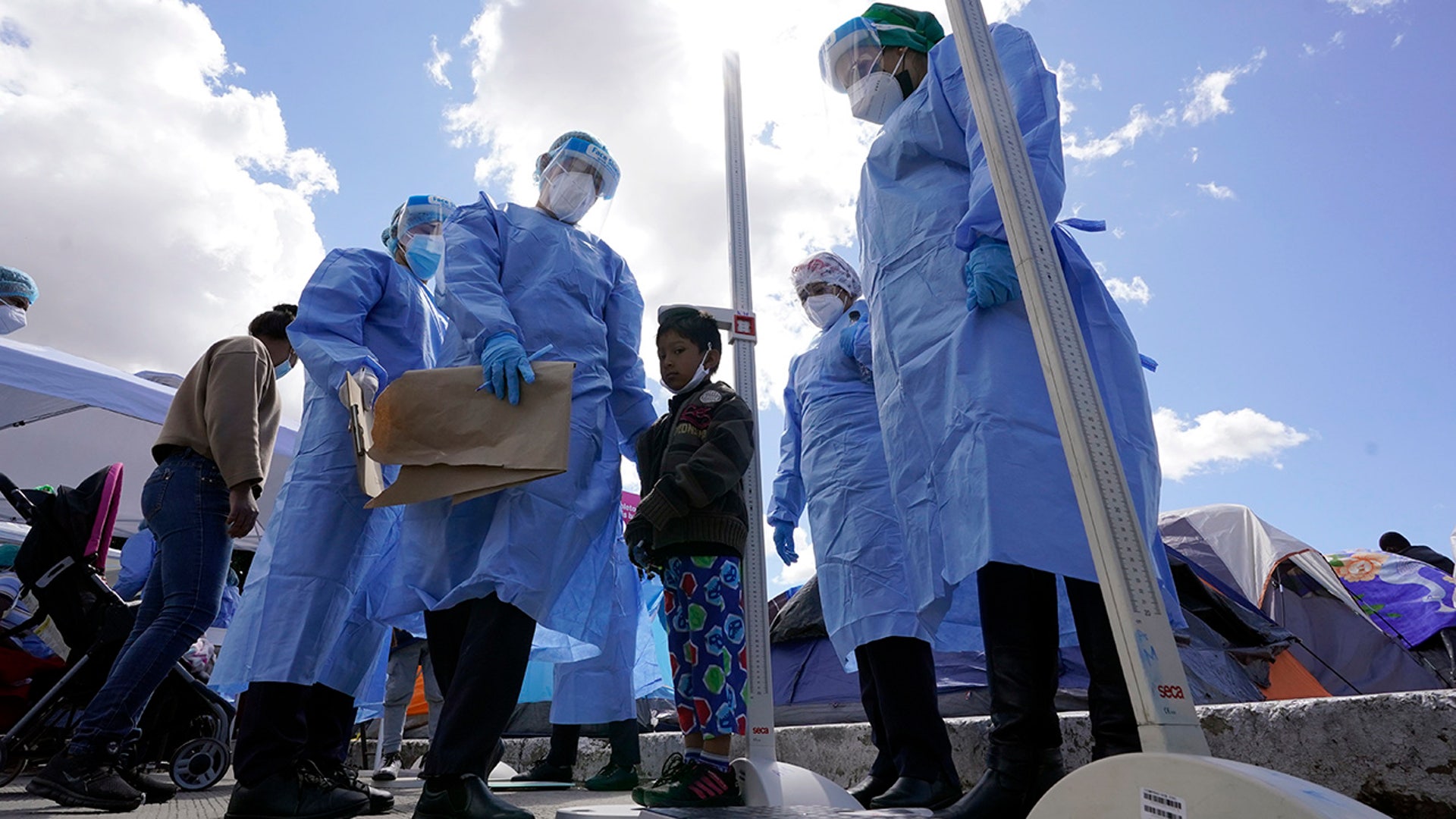 Baja California state health workers measure the height of a boy at a makeshift camp for migrants seeking asylum in the United States at the border crossing Friday, March 12, 2021, in Tijuana, Mexico. The Biden administration hopes to relieve the strain of thousands of unaccompanied children coming to the southern border by terminating a 2018 Trump-era order that discouraged potential family sponsors from coming forward to house the children. (AP Photo/Gregory Bull)