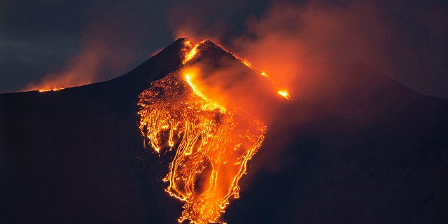 The moon is partially seen in the sky as lava flows from the Mt. Etna volcano, near Catania in Sicily, southern Italy, early Tuesday, Feb. 23 , 2021. (AP Photo/Salvatore Allegra)