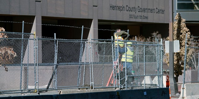 Workers install barbed wire on fencing outside the Hennepin County Government Center, Wednesday, Feb. 23, 2021 in Minneapolis, as part of security preparation for the trial of former Minneapolis police officer Derek Chauvin. (AP Photo/Jim Mone)