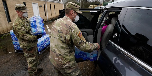 Mississippi Army National Guard Sgt. Chase Toussaint, right, and Staff Sgt. Matthew Riley, both with the Maneuver Area Training Equipment Site of Camp Shelby, place bottled water into a vehicle, Monday, March 1, 2021, in Jackson, Miss. (Associated Press)