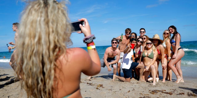 FILE - In this March 17, 2020, file photo, group of spring break revelers pose for a photograph on the beach in Pompano Beach, Fla. Colleges around the U.S. are scaling back spring break or canceling it entirely to discourage beachfront partying that could raise infection rates back on campus. (AP Photo/Julio Cortez, File)