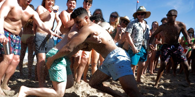 FILE - In this March 17, 2020, file photo, two men wrestle each other as spring break revelers look on during a contest on the beach in Pompano Beach, Fla.