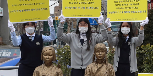 In this Feb. 25, 2021, photo, high school students hold up banners to protest a recent academic paper by Harvard University professor J. Mark Ramseyer, behind statues symbolizing wartime sex slaves in Seoul, South Korea. The signs read: "J. Mark Ramseyer, are you a 21st century professor at Harvard? Are you a university professor in the Japanese Empire 100 years ago? We criticize anti-human rights research." (Lee Jung-hoon/Yonhap via AP)