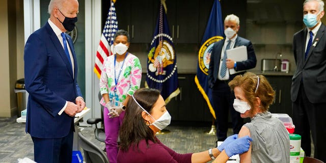 President Joe Biden, standing left, visits a COVID-19 vaccination site and watches Dr. Navjit Goraya administer a vaccine to the Air Force Colonel. 