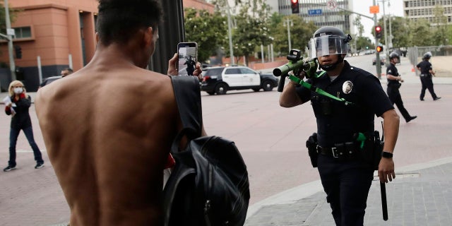 FILE - In this June 2, 2020, file photo, a police officer aims his less-lethal weapon at a demonstrator during a protest in Los Angeles, over the death of George Floyd on May 25 while in police custody in Minneapolis. (AP Photo/Jae C. Hong, File)