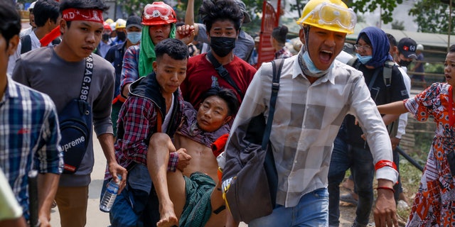 Anti-coup protesters carry an injured man following clashes with security in Yangon, Burma Sunday, March 14, 2021. The civilian leader of Burma's government in hiding vowed to continue supporting a "revolution" to oust the military that seized power in last month's coup, as security forces again met protesters with lethal forces, killing several people. (AP Photo)
