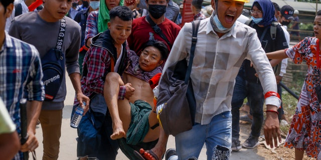 Anti-coup protesters carry an injured man following clashes with security in Yangon, Burma Sunday, March 14, 2021. The civilian leader of Burma's government in hiding vowed to continue supporting a "revolution" to oust the military that seized power in last month's coup, as security forces again met protesters with lethal forces, killing several people. (AP Photo)