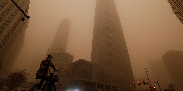 Un cycliste et des automobilistes passent devant des immeubles de bureaux au milieu d'une tempête de sable à l'heure de pointe du matin dans le quartier central des affaires de Pékin le lundi 15 mars 2021. La tempête de sable a apporté une brume colorée dans le ciel de Pékin et lundi les indices de qualité de l'air ont grimpé en flèche.  (Photo AP / Andy Wong)