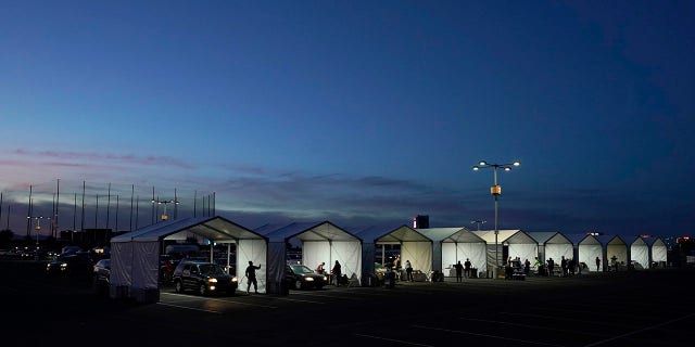 In this Jan. 12, 2021, file photo, several tents are set up so people who have registered can get their COVID-19 vaccinations as they drive-thru the parking lot of the State Farm Stadium in Glendale, Arizona. (AP Photo/Ross D. Franklin)