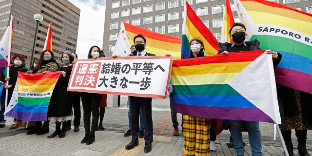 Plaintiffs' lawyers and supporters hold rainbow flags and a banner that reads: "Unconstitutional judgment" outside Sapporo District Court after a court rule, in Sapporo, northern Japan, Wednesday, March 17, 2021. The court ruled the government's ban on same-sex marriages is unconstitutional, recognizing the rights of same-sex couples for the first time in the only Group of Seven country that doesn't acknowledge their legal partnership. (Yohei Fukai/Kyodo News via AP)