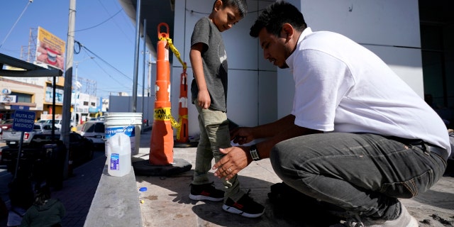 Franklin Reyes, right, a migrant from Honduras, uses a dampened T-shirt to clean the pants of his 7-year-old son, Joshuan Reyes, after they were deported by the U.S. Customs and Border Protection. (AP Photo/Julio Cortez)