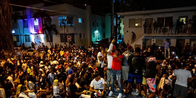 Crowds defiantly gather in the street while a speaker blasts music an hour past curfew in Miami Beach, Fla., on Sunday. An 8 p.m. curfew has been extended in Miami Beach after law enforcement worked to contain unruly crowds of spring break tourists. (Daniel A. Varela/Miami Herald via AP)