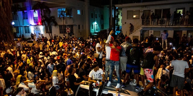 Les foules se rassemblent avec défi dans la rue tandis qu'un orateur diffuse de la musique une heure après le couvre-feu à Miami Beach, en Floride, dimanche.  Un couvre-feu de 20 heures a été prolongé à Miami Beach après que les forces de l'ordre aient travaillé pour contenir les foules indisciplinées de touristes pendant les vacances de printemps.  (Daniel A. Varela / Miami Herald via AP)