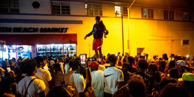 Un homme se tient sur une voiture alors que les foules se rassemblent avec défi dans la rue tandis qu'un haut-parleur diffuse de la musique une heure après le couvre-feu à Miami Beach, en Floride, le dimanche 21 mars 2021. 