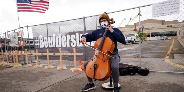 Louis Saxton plays his cello by a fence put up around the parking lot where a mass shooting took place in a King Soopers grocery store Tuesday, March 23, 2021, in Boulder, Colo. (AP Photo/David Zalubowski)