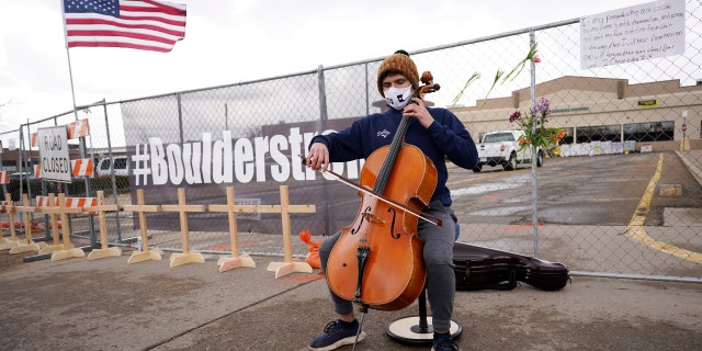Louis Saxton plays his cello by a fence put up around the parking lot where a mass shooting took place in a King Soopers grocery store Tuesday, March 23, 2021, in Boulder, Colo. (AP Photo/David Zalubowski)