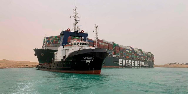In this photo released by the Suez Canal Authority, a boat sails in front of a huge freighter, named MV Ever Given, at the back, is immobilized on Wednesday, March 24, 2021 (Credit: Suez Canal Authority via AP)