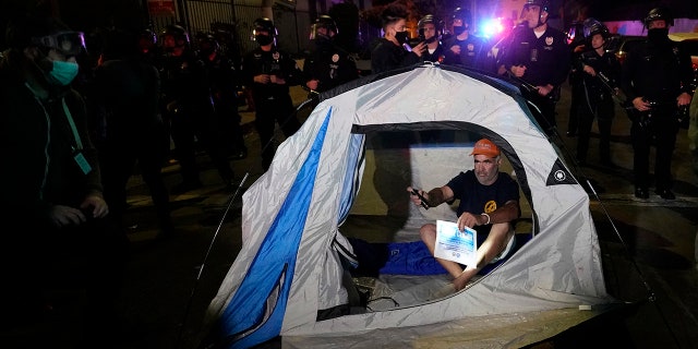 A demonstrator sets up a tent in front of police in the Echo Park section of Los Angeles Thursday, March 25, 2021. Demonstrators gathered to protest the planned temporary closure of a Los Angeles park that would displace a large homeless encampment, which has grown throughout the coronavirus pandemic. 