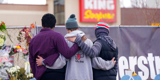 Des personnes en deuil se consolent le long de la clôture temporaire à l'extérieur du parking d'une épicerie King Soopers, site d'une fusillade de masse au cours de laquelle 10 personnes sont mortes, le vendredi 26 mars 2021, à Boulder, au Colorado. 