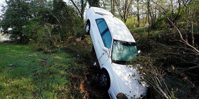 A car that was carried by floodwaters leans against a tree in a creek Sunday, March 28, 2021, in Nashville, Tenn. Heavy rain across Tennessee flooded homes and roads as a line of severe storms crossed the state. (AP Photo/Mark Humphrey)