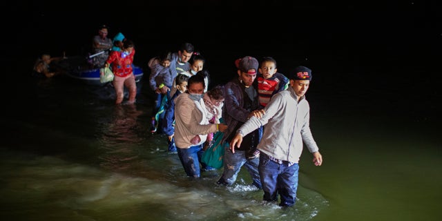 Migrant families, mostly from Central American countries, wade through shallow waters after being delivered by smugglers on small inflatable rafts on U.S. soil in Roma, Texas, Wednesday, March 24, 2021. As soon as the sun sets, at least 100 migrants crossed through the Rio Grande river by smugglers into the United States. (AP Photo/Dario Lopez-Mills)