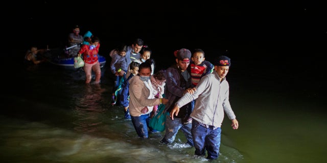 Migrant families, mostly from Central American countries, wade through shallow waters after being delivered by smugglers on small inflatable rafts on U.S. soil in Roma, Texas, Wednesday, March 24, 2021. As soon as the sun sets, at least 100 migrants crossed through the Rio Grande river by smugglers into the United States. (AP Photo/Dario Lopez-Mills)