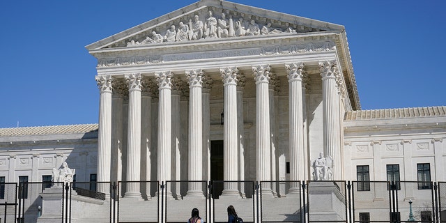 FILE - In this March 21, 2021, file photo people view the Supreme Court building from behind security fencing on Capitol Hill in Washington after portions of an outer perimeter of fencing were removed overnight to allow public access.  (AP Photo/Patrick Semansky, File)