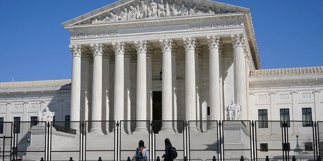 FILE - In this March 21, 2021, file photo people view the Supreme Court building from behind security fencing on Capitol Hill in Washington after portions of an outer perimeter of fencing were removed overnight to allow public access.  (AP Photo/Patrick Semansky, File)