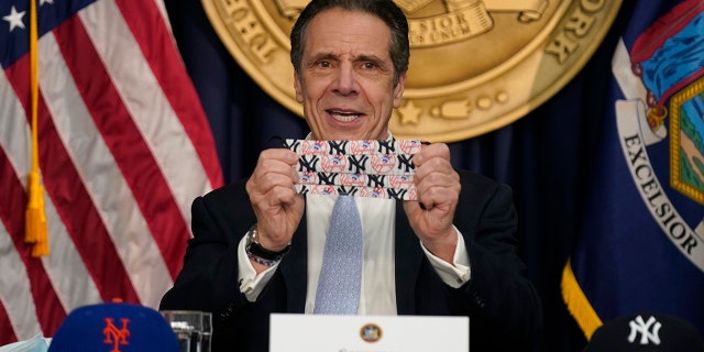 New York Governor Andrew Cuomo shows off a mask that has both New York Yankees and New York Mets logos during an event at his office in New York, Thursday, March 18, 2021. 