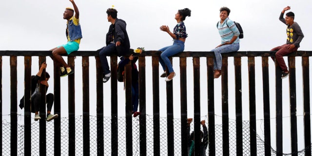 Central American migrants sit on top of the border wall.