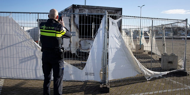 FILE - In this Jan. 24, 2021, file photo, a police officer takes pictures of a burned-out coronavirus testing facility in the fishing village of Urk in the Netherlands after it was set on fire the night before by rioting youths protesting on the first night of a nationwide curfew. (AP Photo/Peter Dejong, File)