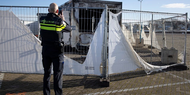 FILE - In this Jan. 24, 2021, file photo, a police officer takes pictures of a burned-out coronavirus testing facility in the fishing village of Urk in the Netherlands after it was set on fire the night before by rioting youths protesting on the first night of a nationwide curfew. (AP Photo/Peter Dejong, File)