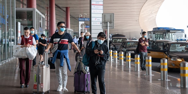 Travelers wearing protective masks push their luggage outside Beijing Capital International Airport in Beijing, China, on Wednesday, Sept. 30, 2020. (Yan Cong/Bloomberg via Getty Images)