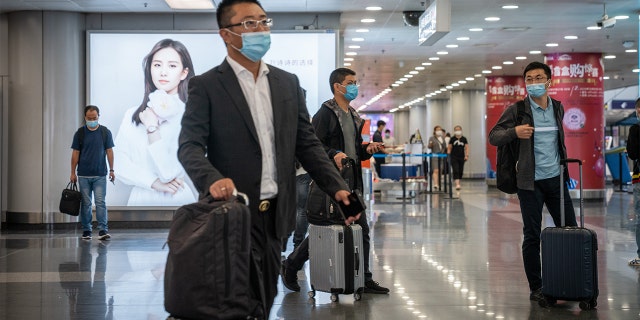 Travelers wearing protective masks push their luggage through Beijing Capital International Airport in Beijing, China, on Wednesday, Sept. 30, 2020. (Yan Cong/Bloomberg via Getty Images)