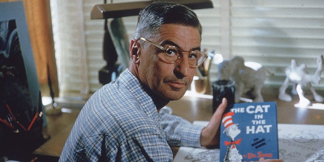 The American author and illustrator Dr.  Seuss (Theodor Seuss Geisel, 1904-1991) sits at his set-up table in his home office with a copy of his book, "The cat in the hat," La Jolla, California, April 25, 1957. (Photo by Gene Lester / Getty Images)