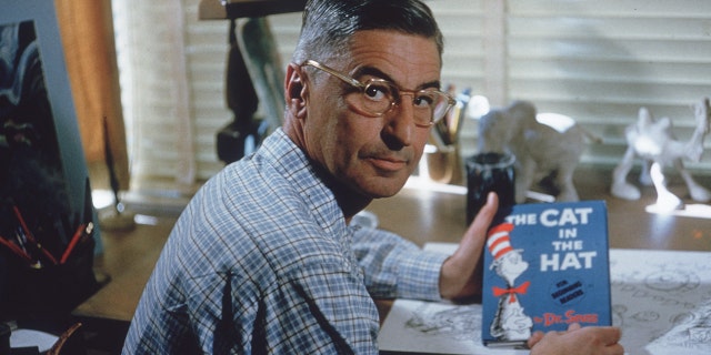 The American author and illustrator Dr.  Seuss (Theodor Seuss Geisel, 1904-1991) sits at his set-up table in his home office with a copy of his book, "The cat in the hat," La Jolla, California, April 25, 1957. (Photo by Gene Lester / Getty Images)