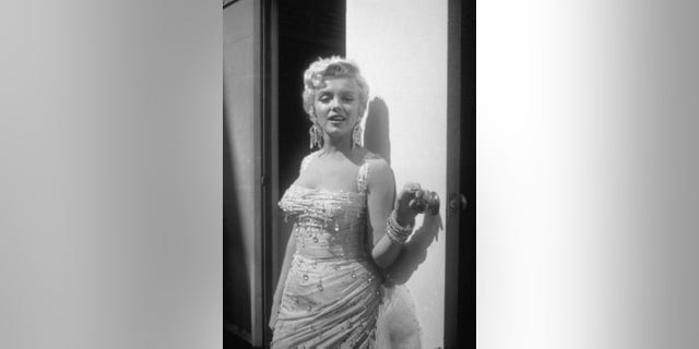 Portrait of Marilyn Monroe in a light-colored, beaded gown, as she leans against an open trailer door on the 20th Century Fox studios set during the filming of director Walter Lang's film, 'There's No Business Like Show Business,' 1954.