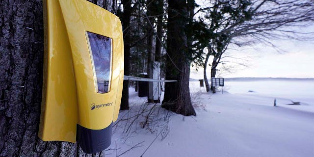 A hand sanitizer dispenser remains mounted to a tree at Camp Fernwood, a summer camp for girls, Saturday, Feb. 20, 2021, in Poland, Maine. (AP Photo/Robert F. Bukaty)