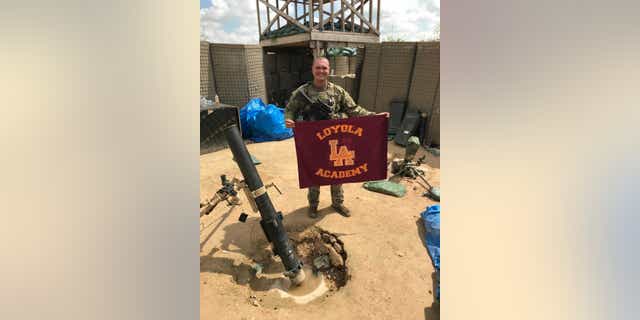 Spc George Kemper holds a Loyola Academy flag while serving in the U.S. Army.